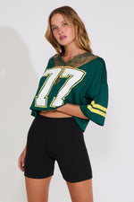 Woman wearing a green sports jersey with the number 77 with black shorts on a white background
