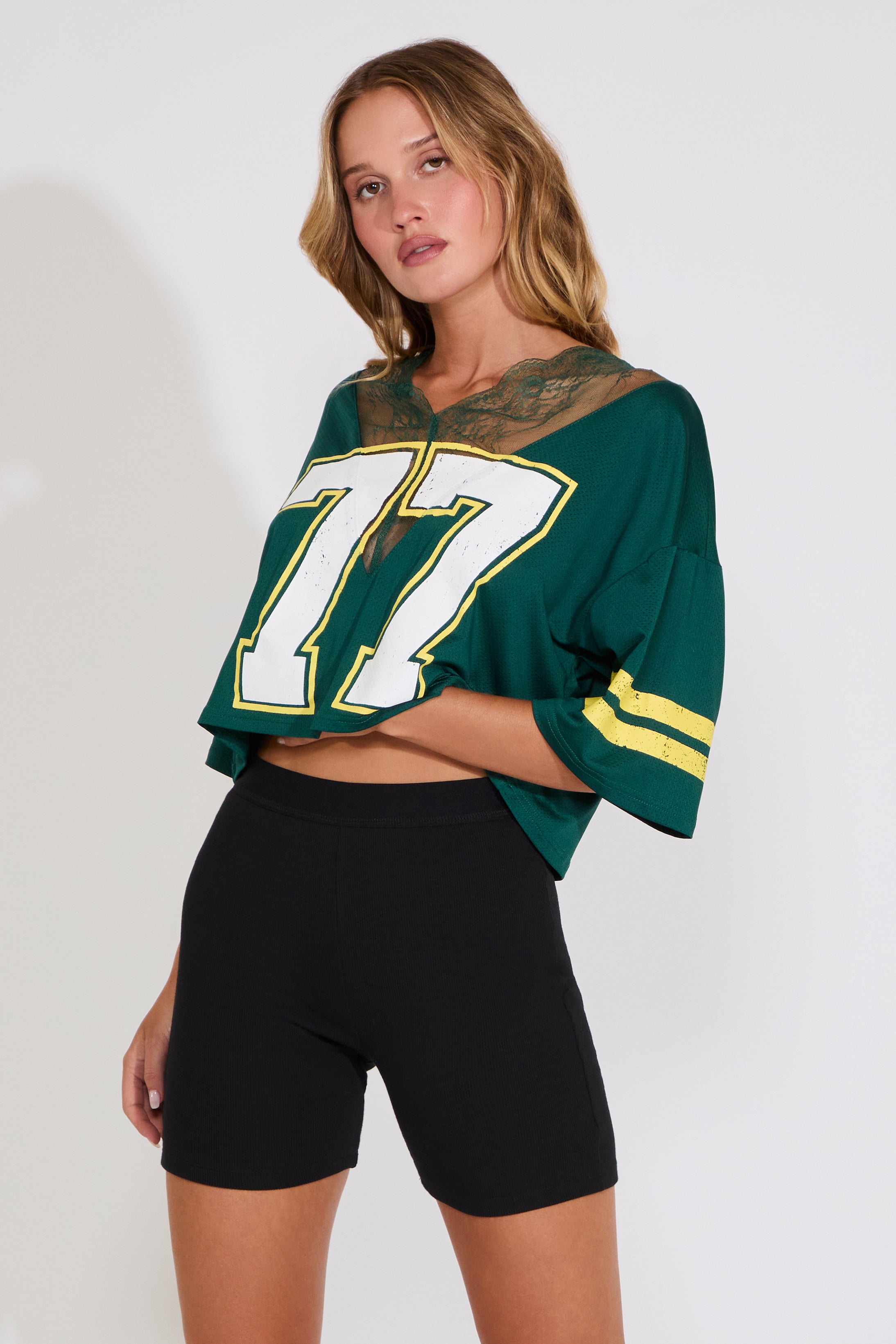 Woman wearing a green sports jersey with the number 77 with black shorts on a white background