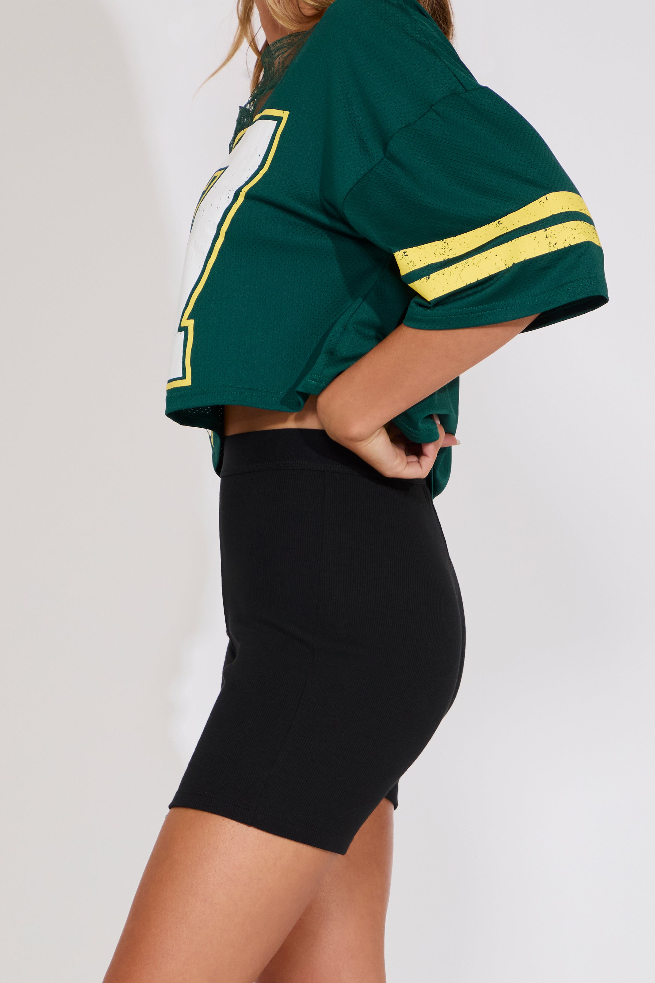 Person wearing a green sports jersey with yellow stripes and black shorts on a white background