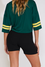 Person wearing a green sports jersey with yellow stripes and black shorts on a white background