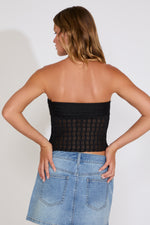 Woman wearing a black tube top and blue jeans against a white background