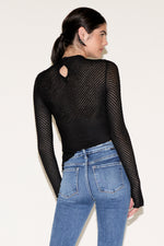 Woman wearing a black mesh long-sleeve top and blue jeans on a white background