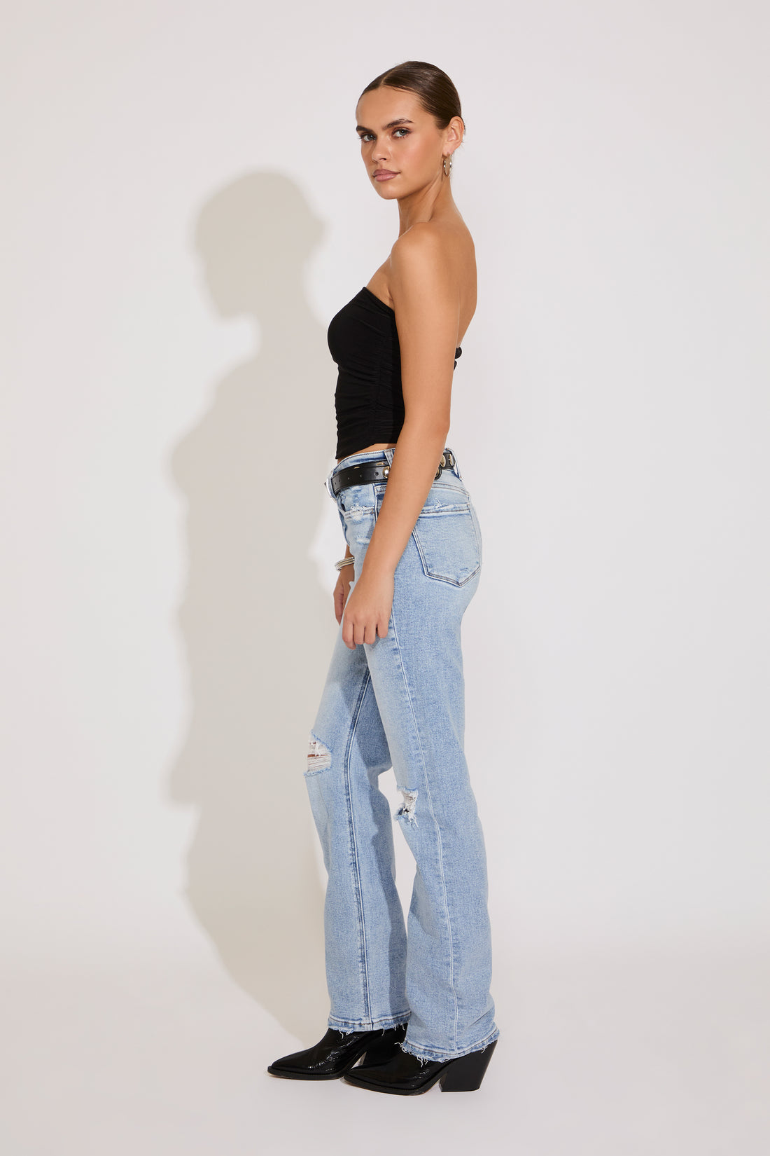 Woman wearing a black strapless top and light blue ripped jeans on a white background