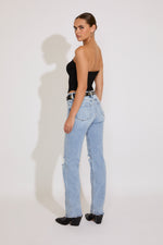 Woman wearing a black strapless top and light blue jeans on a white background