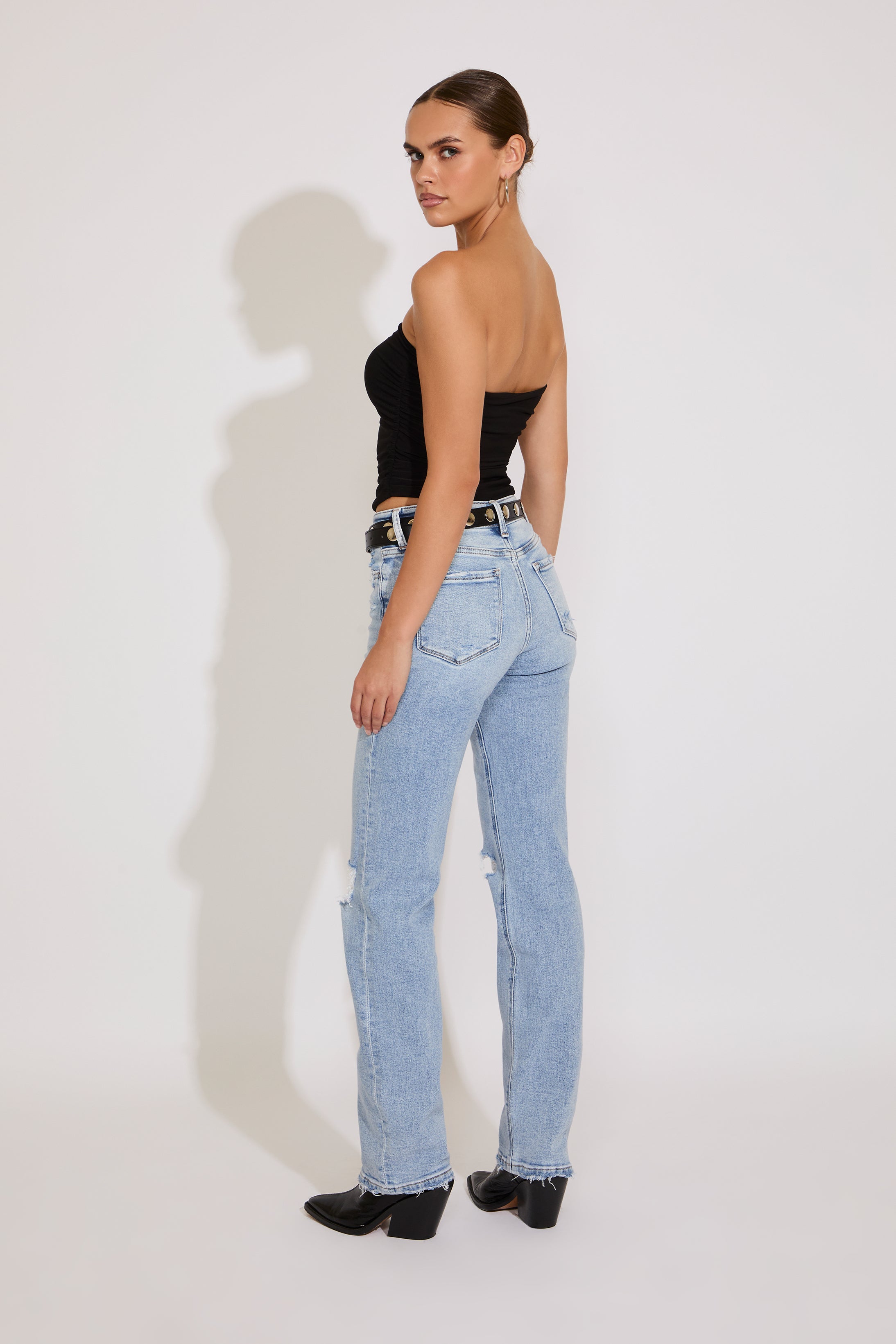 Woman wearing a black strapless top and light blue jeans on a white background
