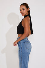Woman wearing a black halter top and blue jeans against a white background