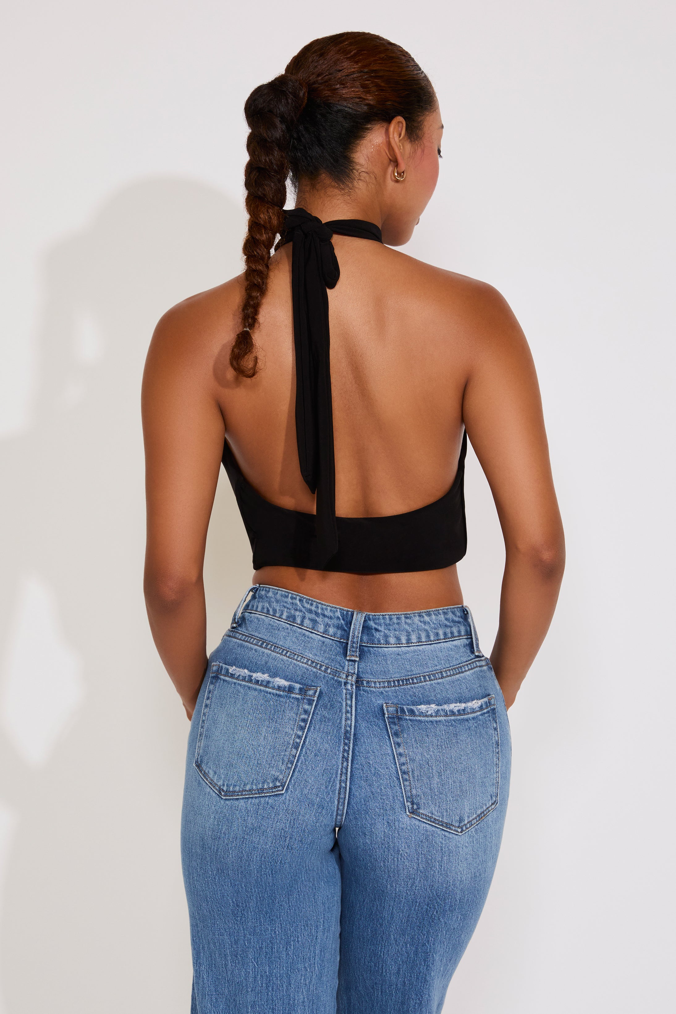 Woman wearing a black halter top with a tie detail and blue jeans on a white background
