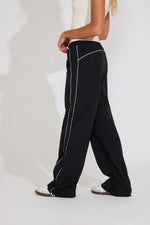 Black pants with white piping worn by a person on a white background