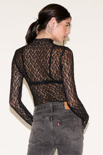 Person wearing a black lace top and gray jeans against a white background