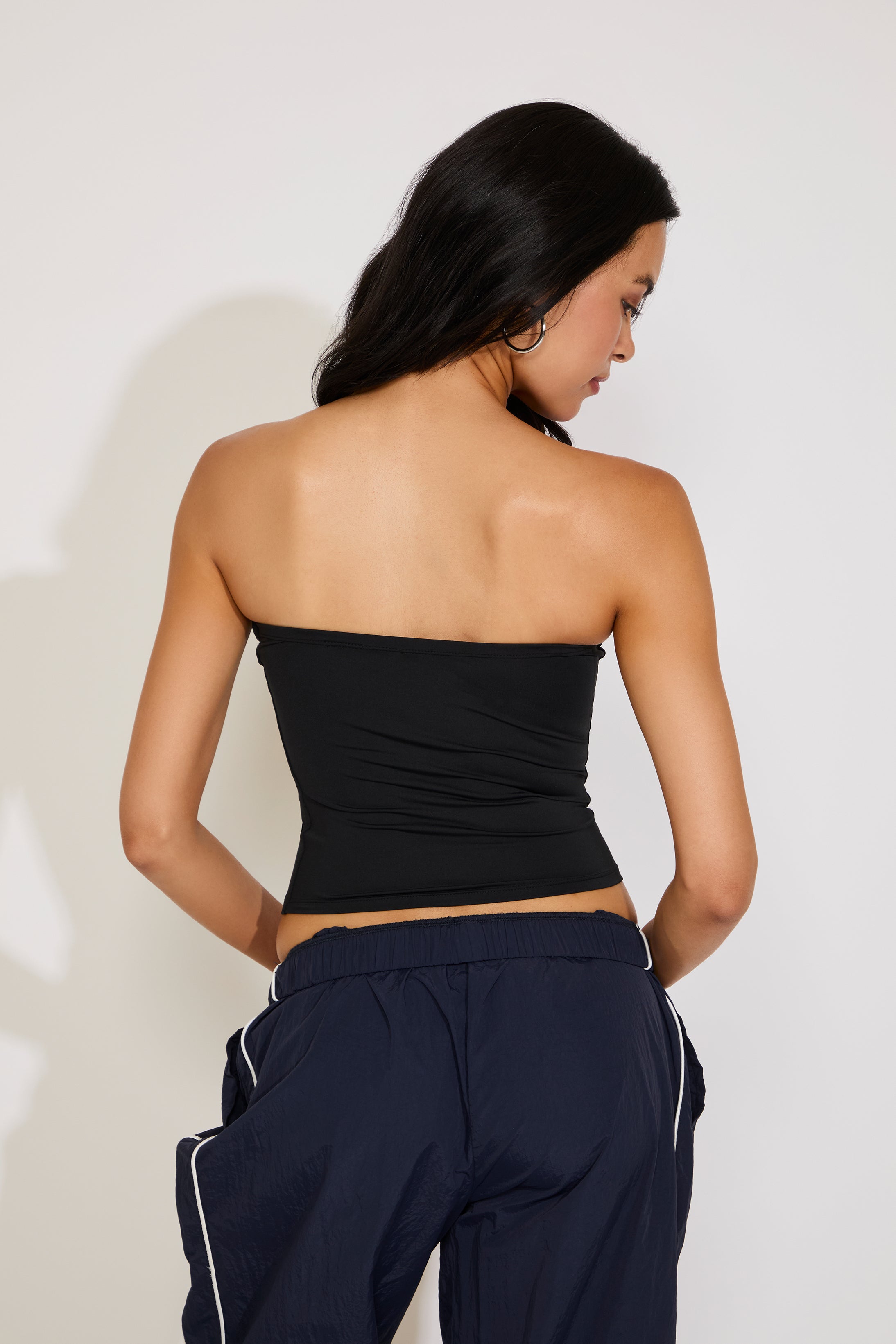 Woman wearing a black strapless top and navy pants against a white background