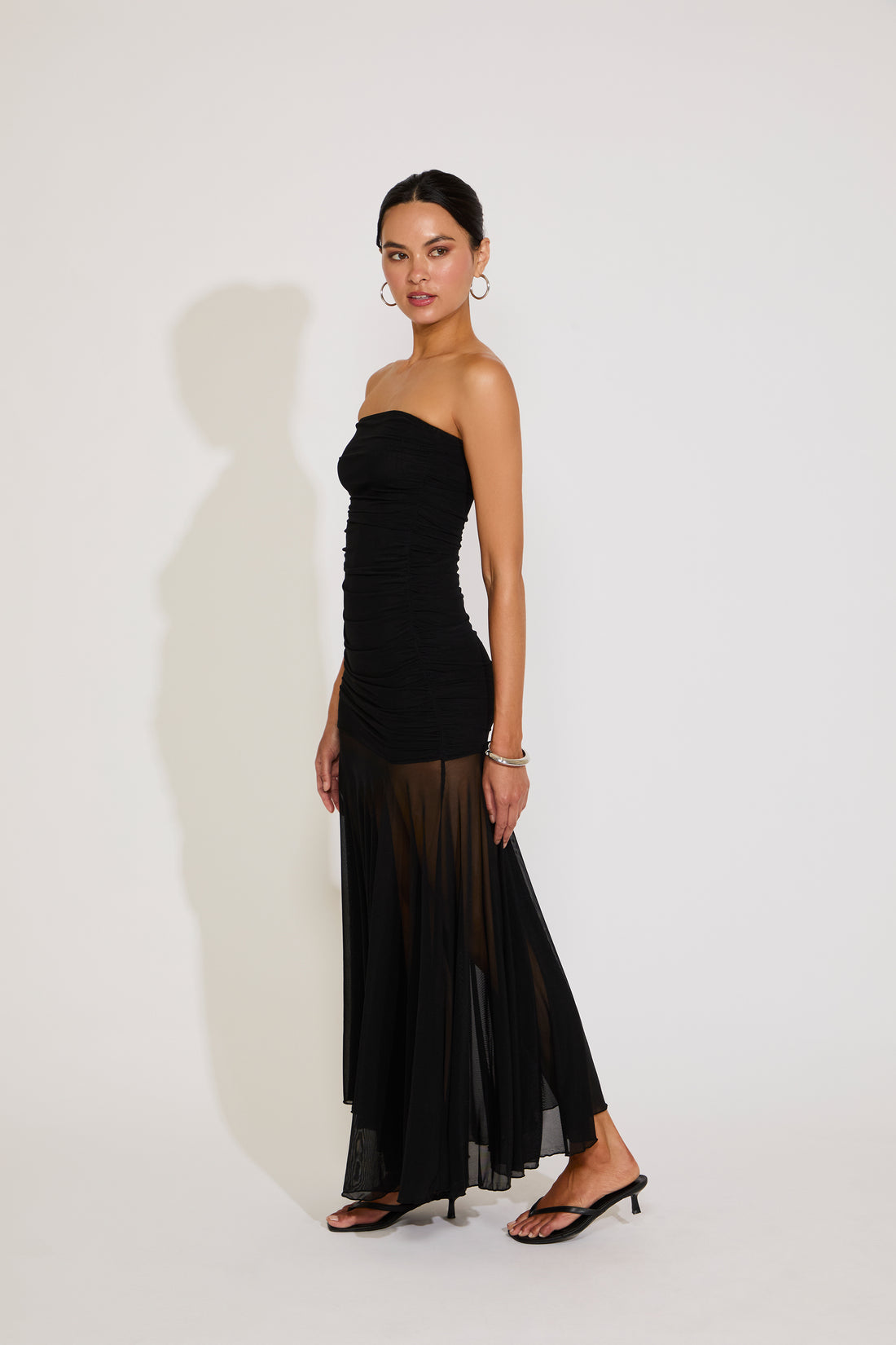 Woman wearing a black strapless dress with sheer overlay on a white background
