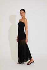 Woman wearing a black strapless dress with sheer overlay on a white background