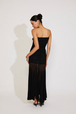 Woman wearing a black strapless dress with sheer overlay on a white background