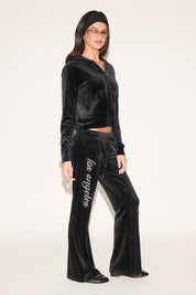 Woman wearing a black velvet tracksuit with 'Los Angeles' text on pants against a white background