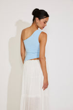 Woman wearing a light blue top and white skirt against a plain background