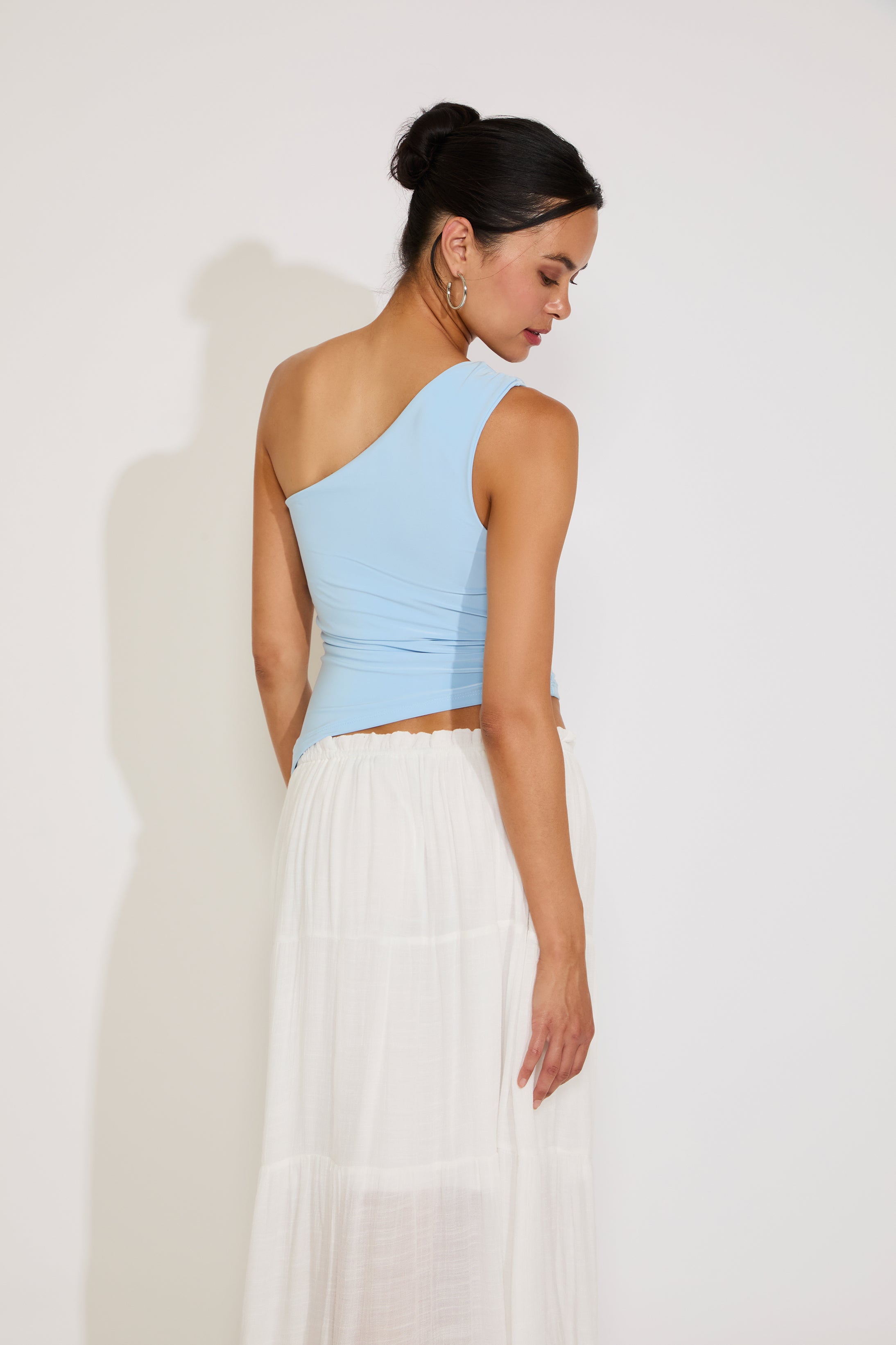 Woman wearing a light blue top and white skirt against a plain background