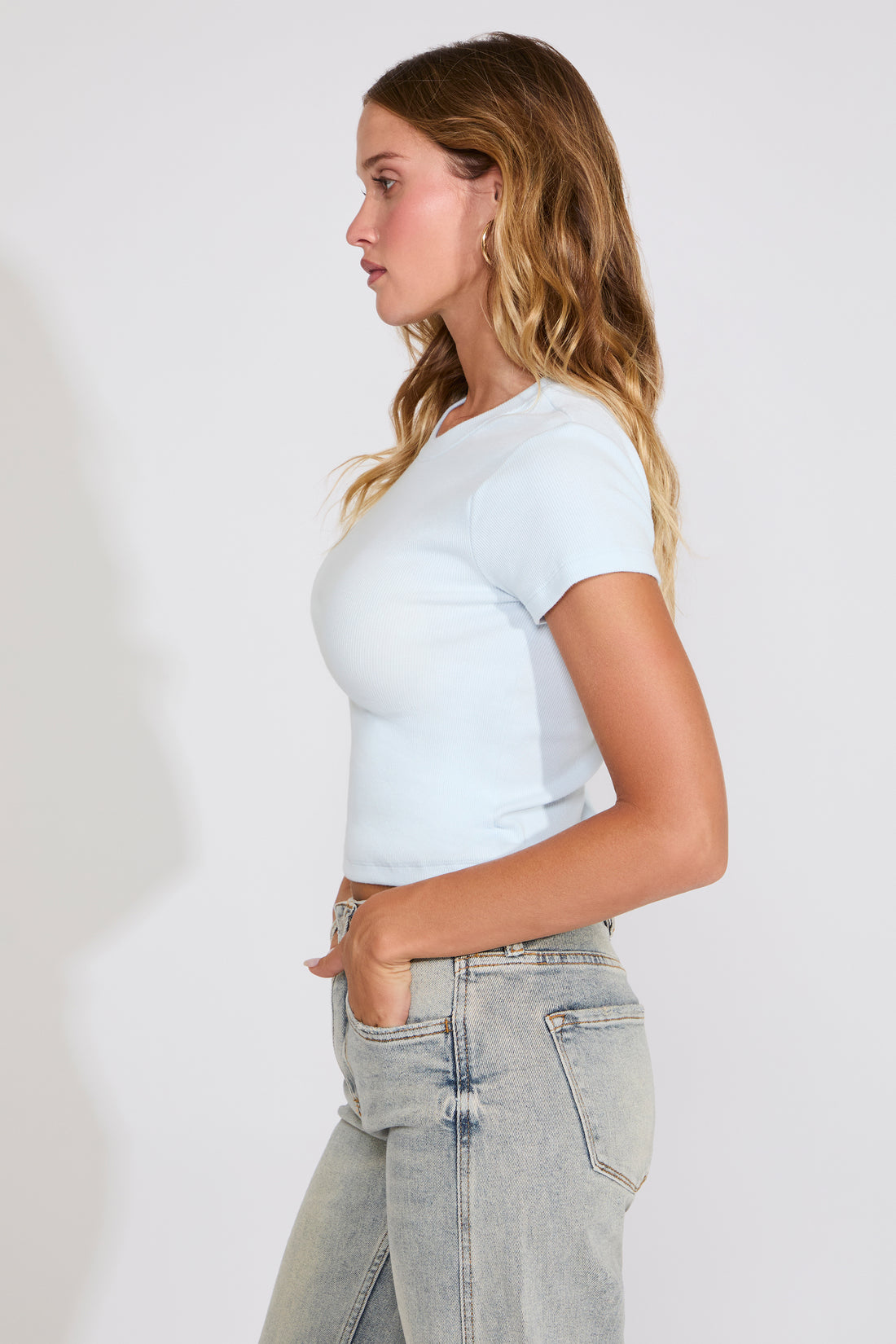 Woman wearing a light blue t-shirt and gray jeans against a plain background