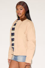 Woman wearing a beige sweater, denim skirt, and patterned headband against a white background