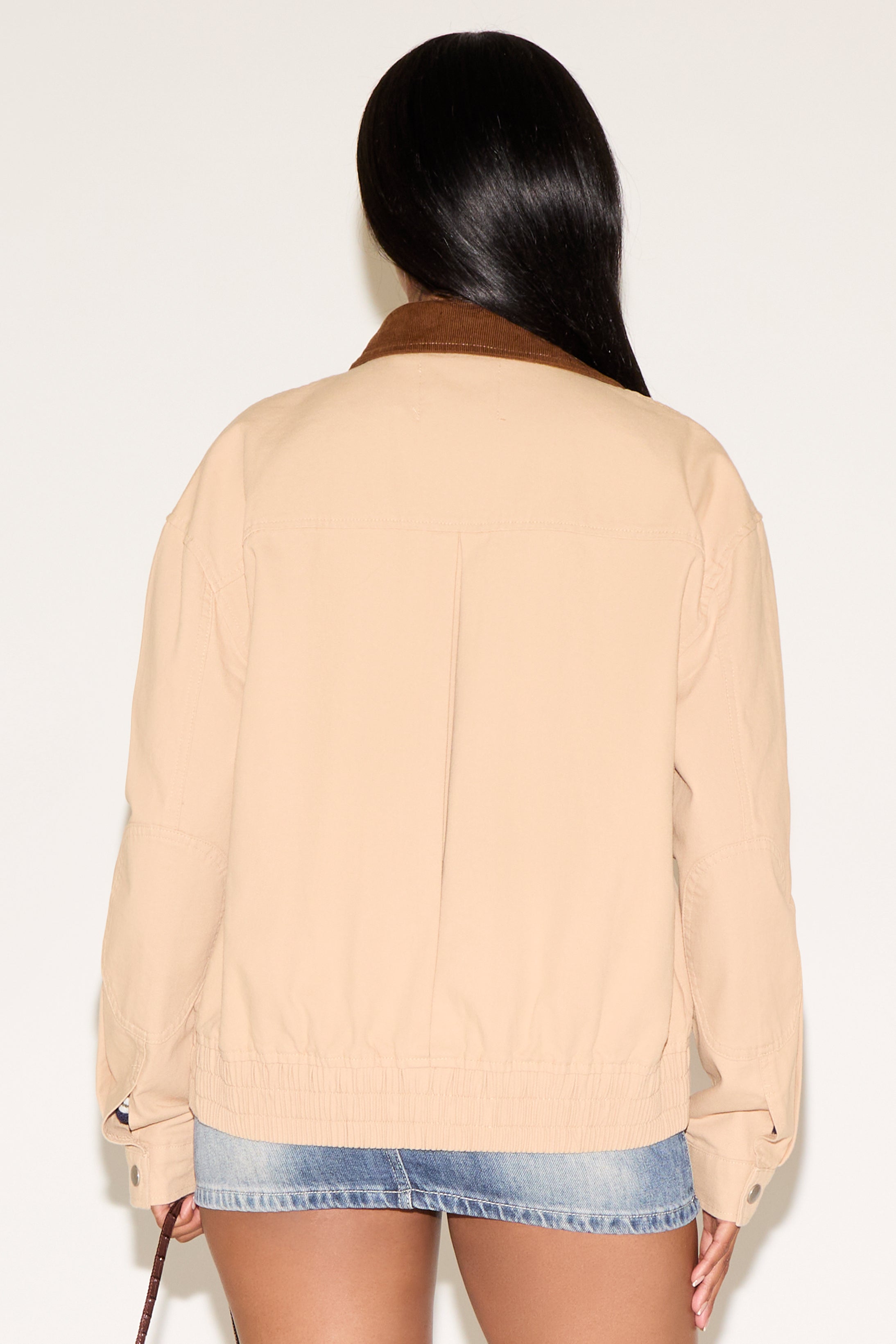 Woman wearing a beige jacket and denim shorts on a plain background