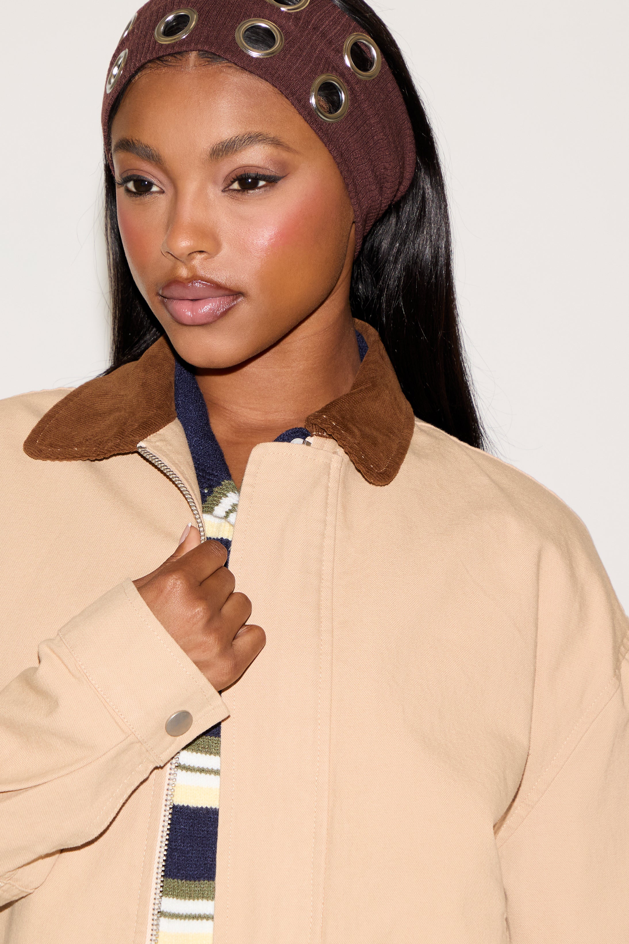 Woman wearing a beige coat with a brown collar and headband against a plain background