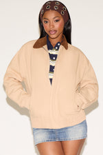 Woman wearing a beige jacket with a brown collar, striped shirt, and denim shorts on a white background