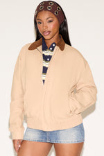 Woman wearing a beige jacket with a brown collar, striped shirt, and denim shorts on a white background
