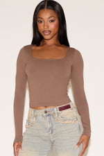 Woman wearing a brown long-sleeve top and light blue jeans on a white background