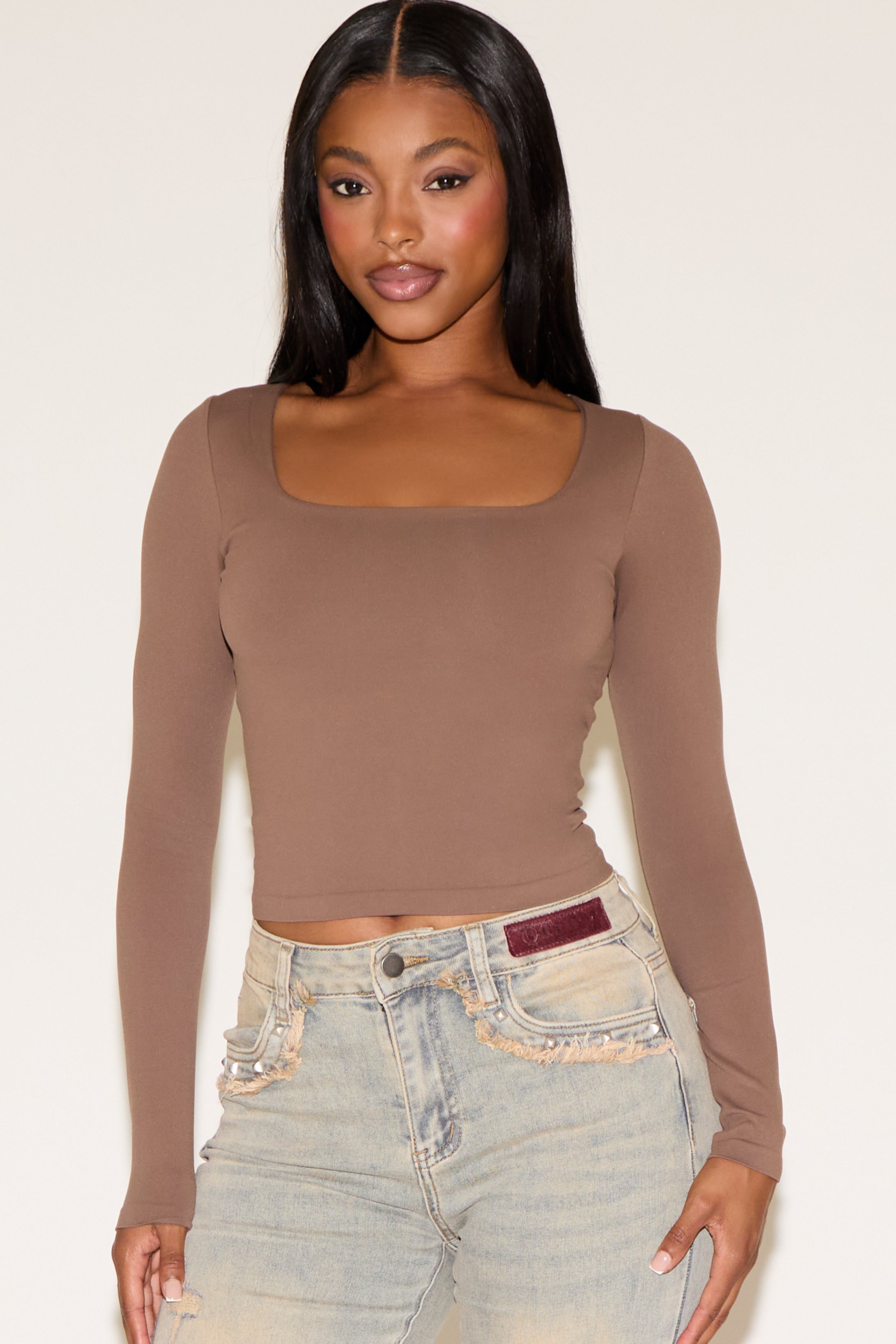 Woman wearing a brown long-sleeve top and light blue jeans on a white background