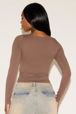 Woman wearing a brown long-sleeve top and light blue jeans against a white background
