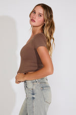 Woman wearing a brown top and light blue jeans against a white background