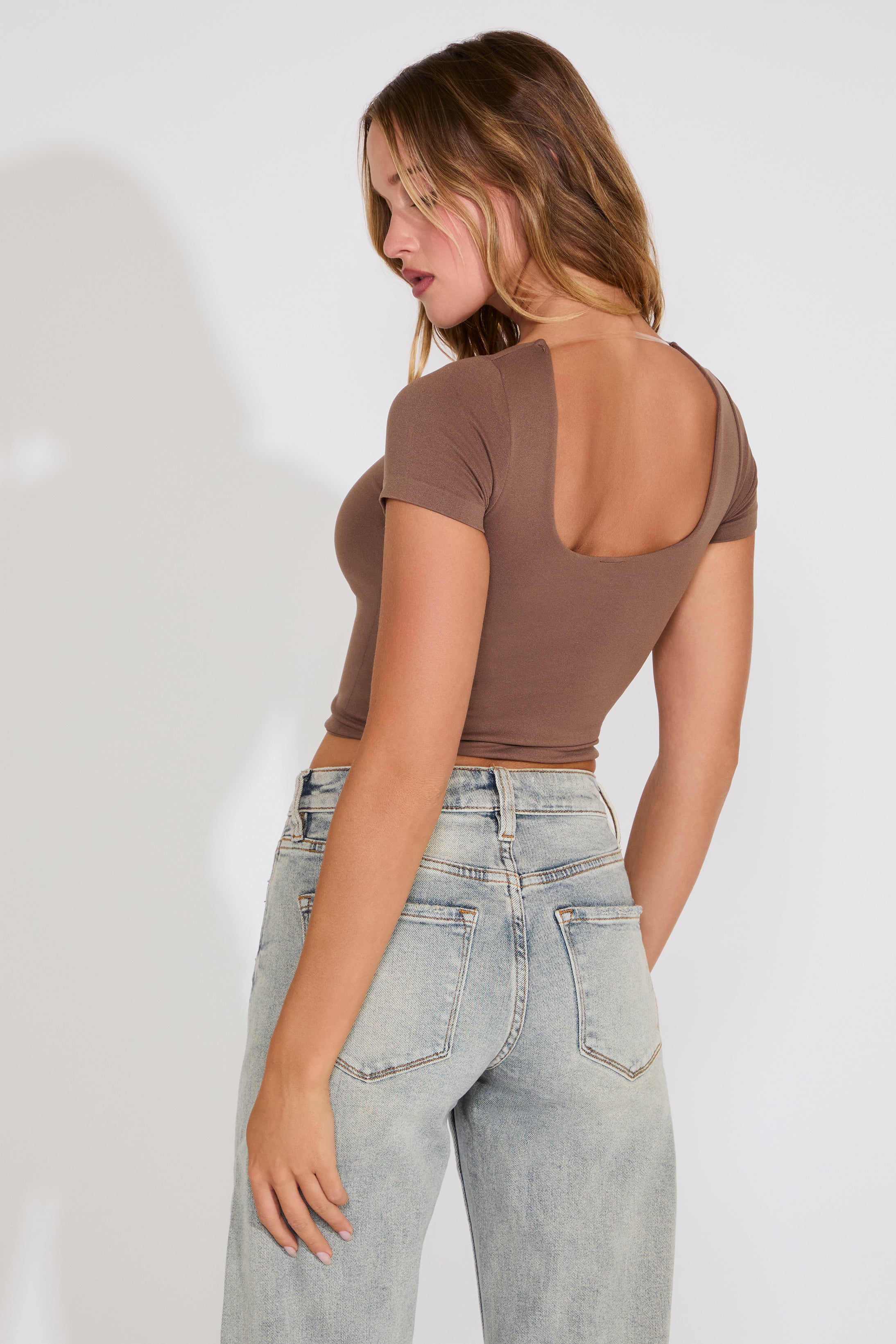Woman wearing a brown open-back top and light blue jeans against a white background