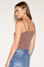 Woman wearing a brown tank top and blue jeans against a plain background