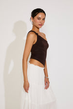 Woman wearing a brown top and white skirt against a plain background
