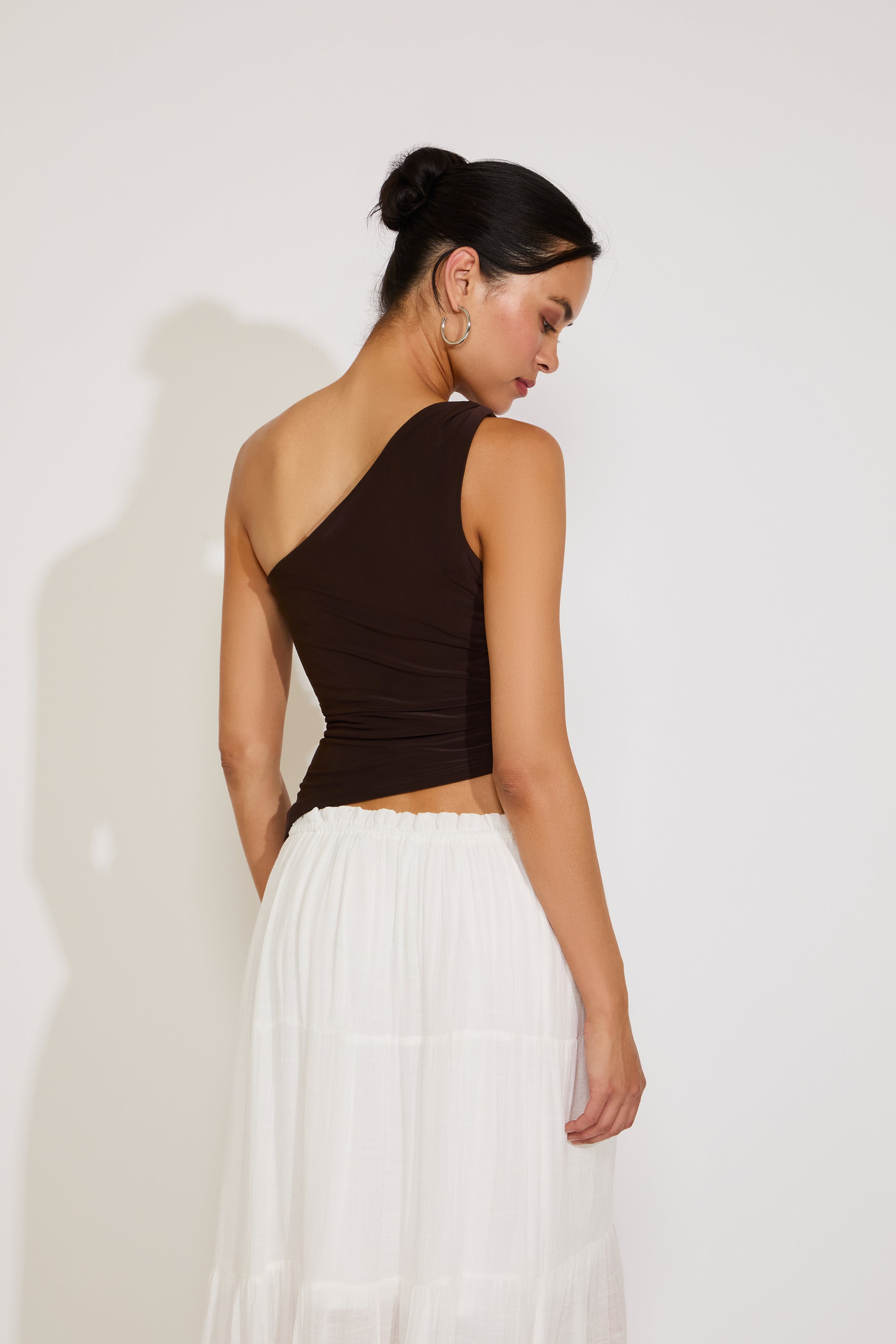 Woman wearing a brown top and white skirt against a plain background