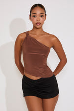 Woman wearing a brown one-shoulder top and black skirt against a white background