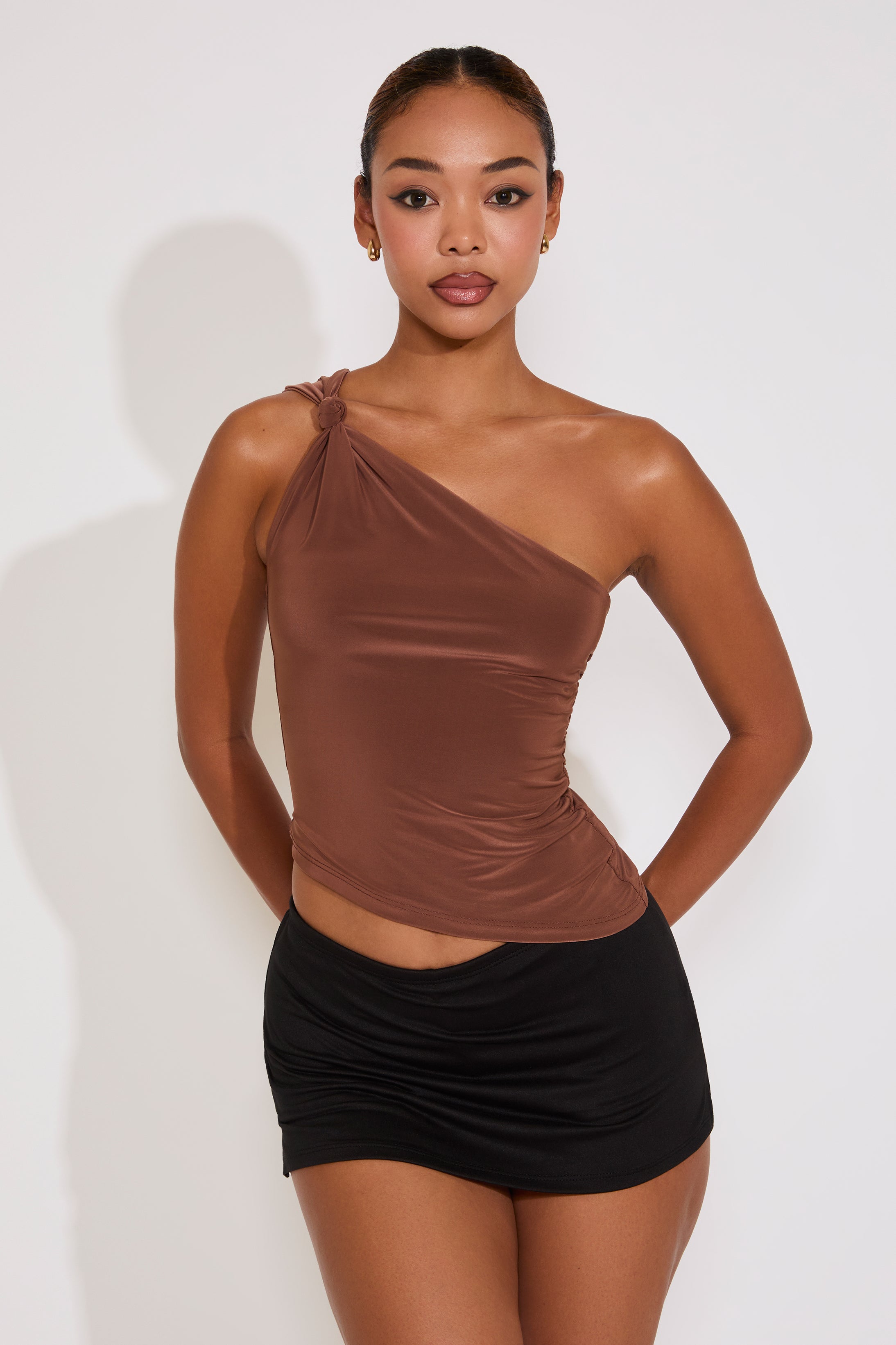 Woman wearing a brown one-shoulder top and black skirt against a white background