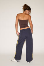 Woman wearing a strapless top and dark blue pants with yellow stripes on a white background