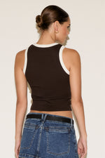 Woman wearing a black tank top and blue jeans against a plain background