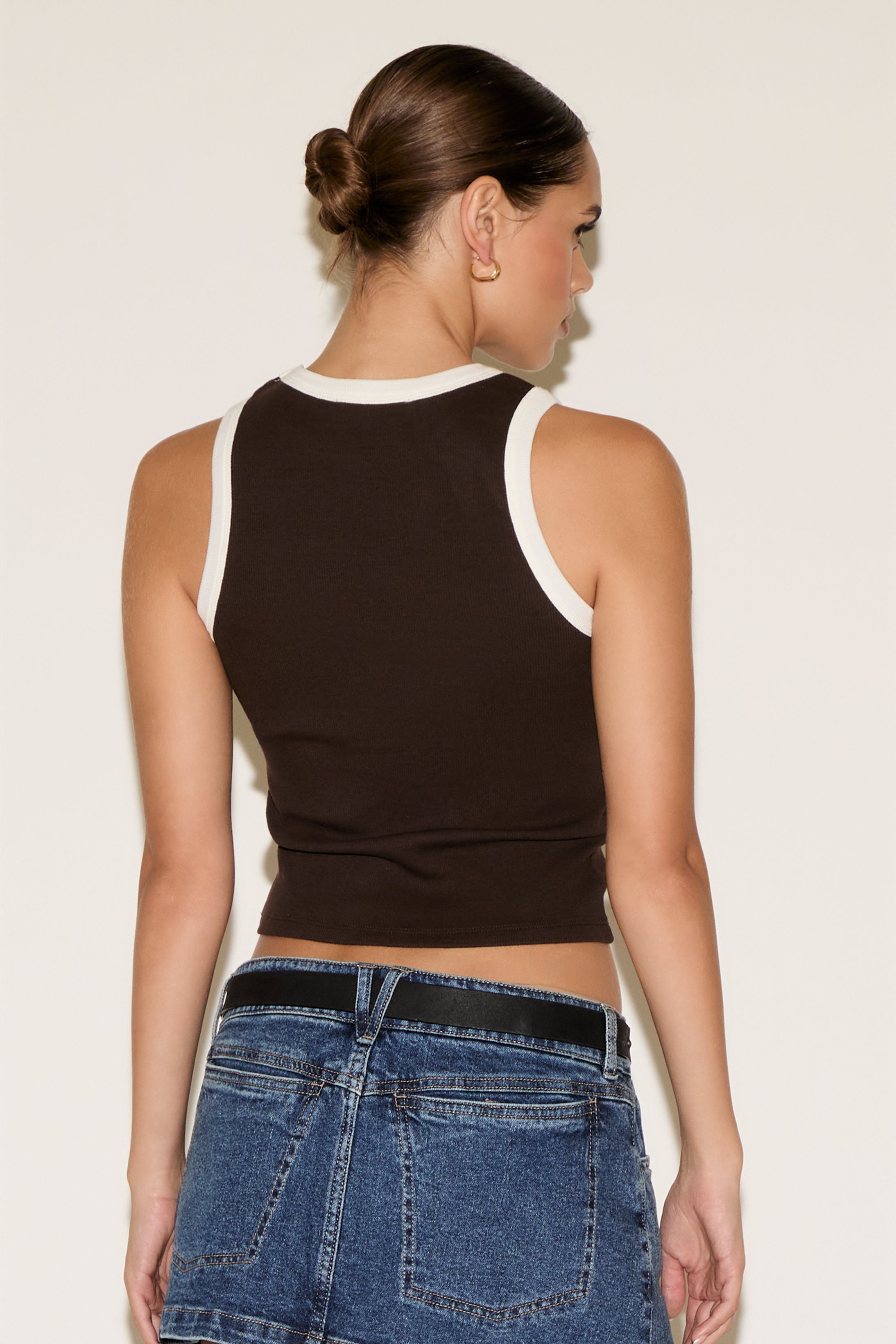 Woman wearing a black tank top and blue jeans against a plain background