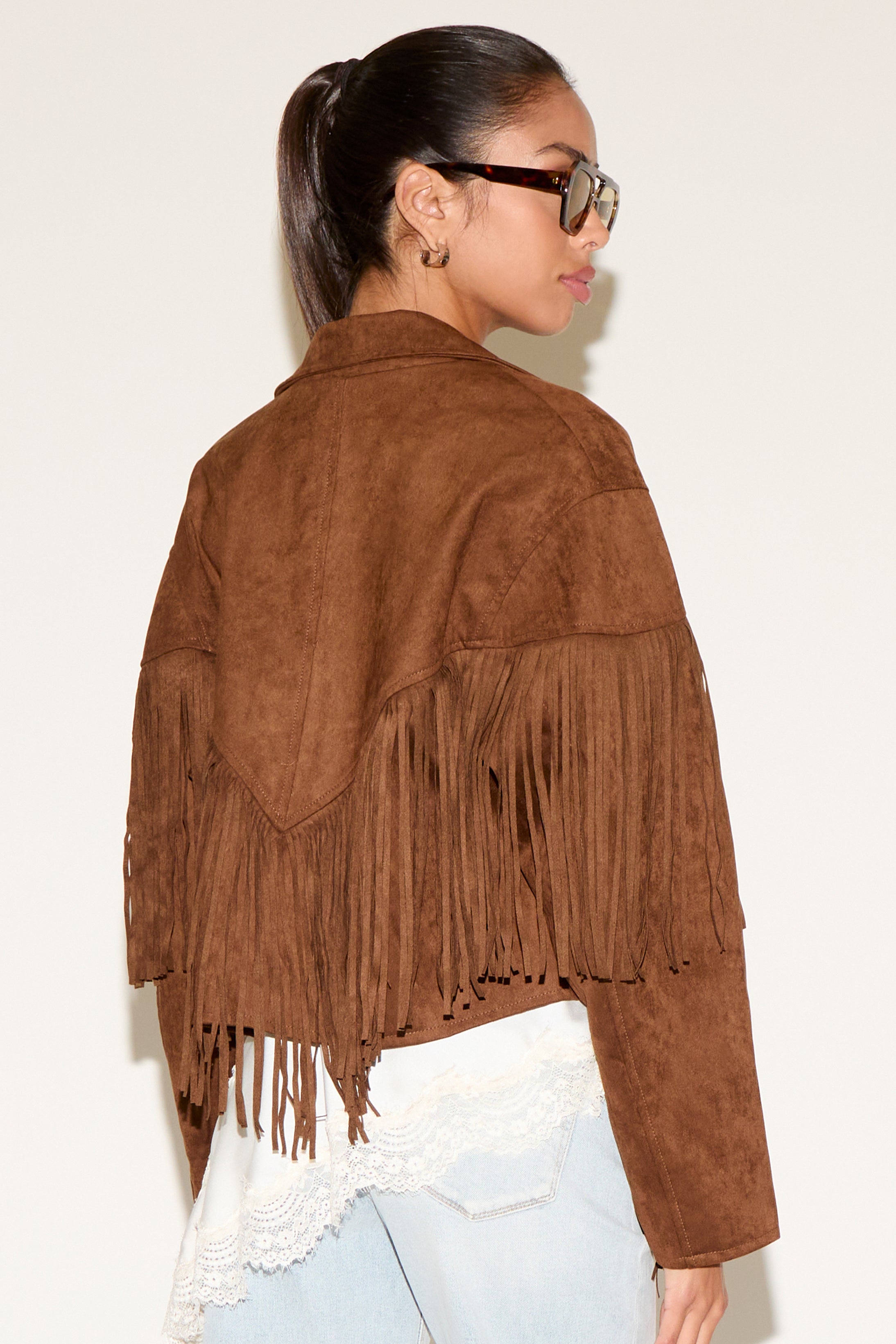 Woman wearing a brown suede jacket with fringes on a plain background