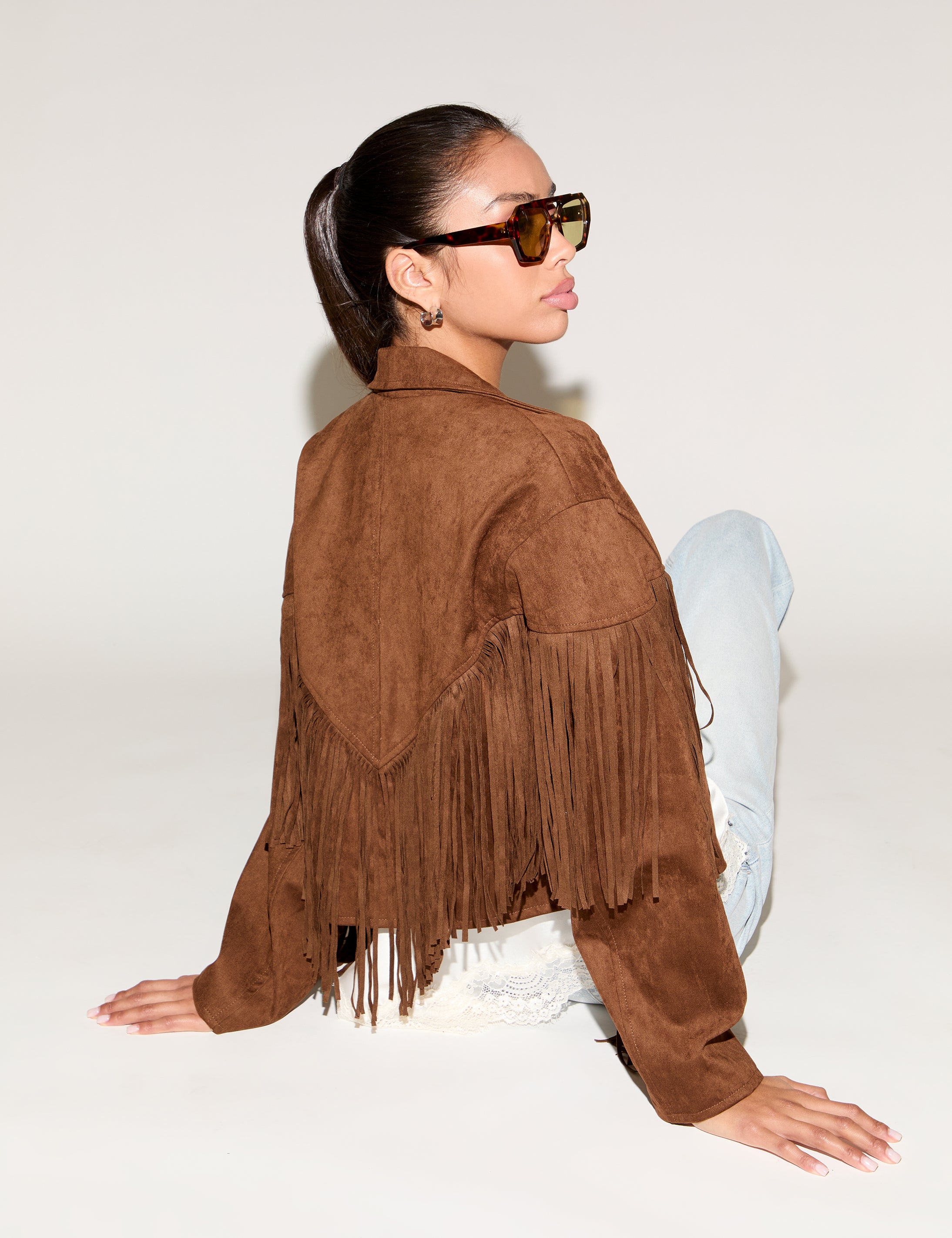 Person wearing a brown suede fringe jacket on a white background