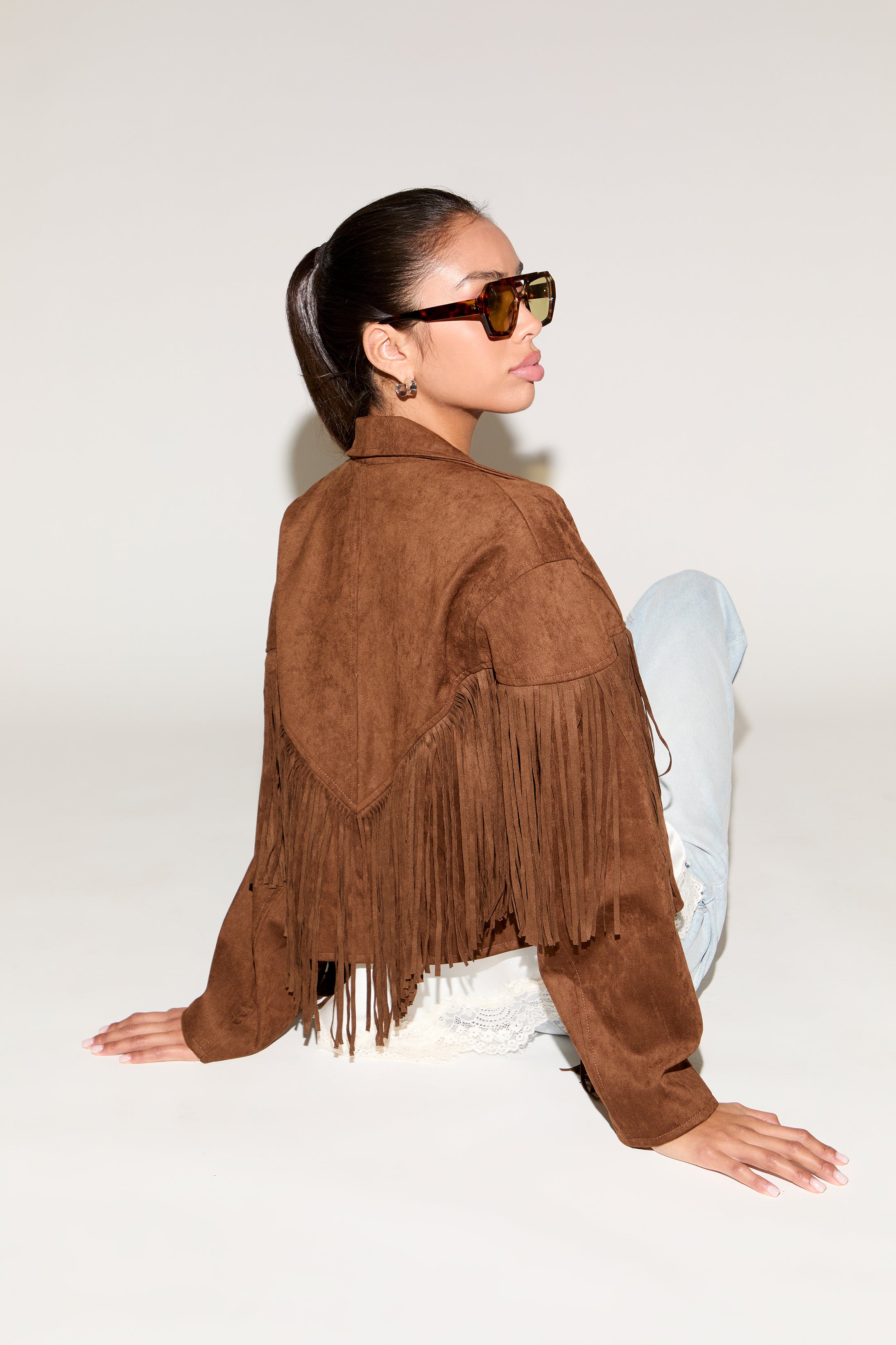 Person wearing a brown suede fringe jacket on a white background