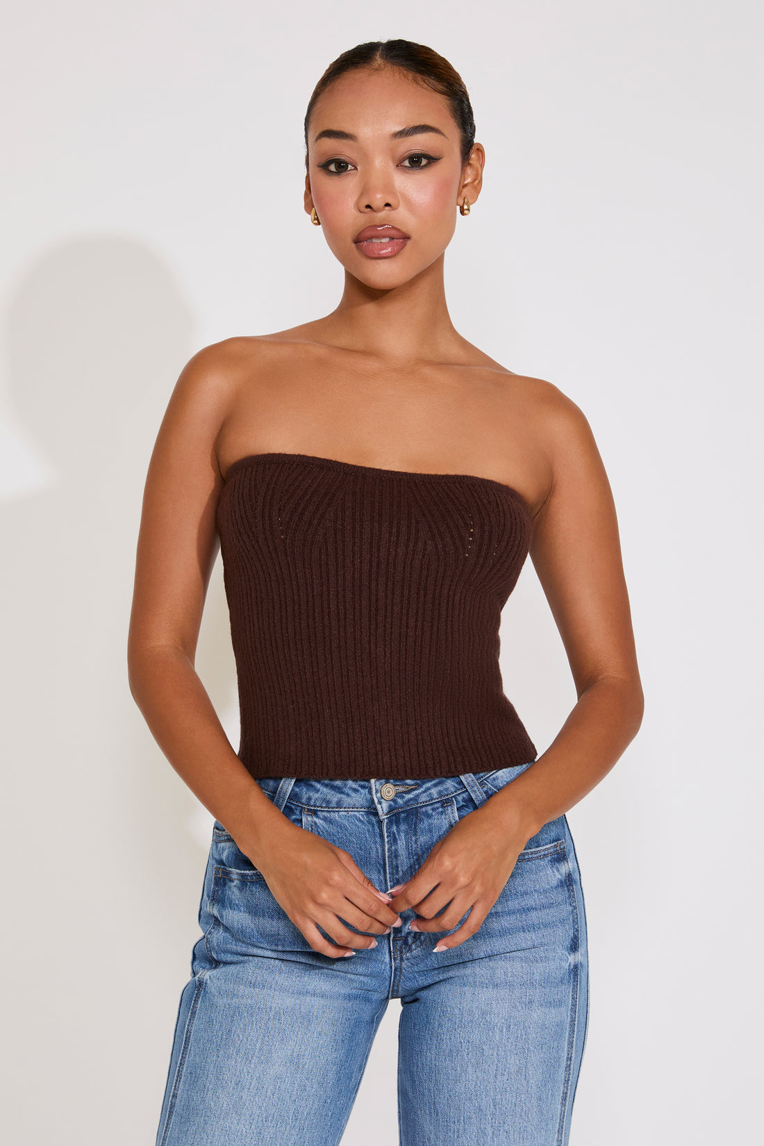 Woman wearing a brown strapless top and blue jeans against a white background