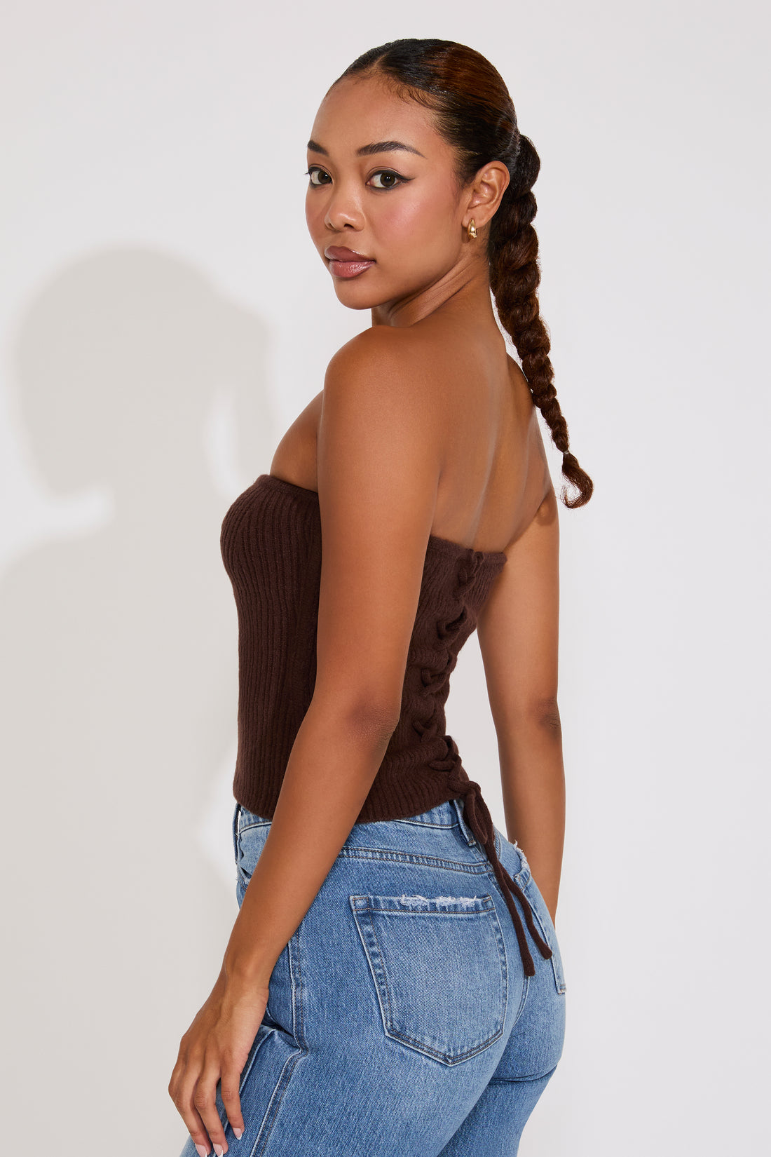 Woman wearing a brown strapless top and blue jeans against a white background