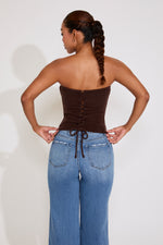 Woman wearing a brown strapless top and blue jeans on a white background