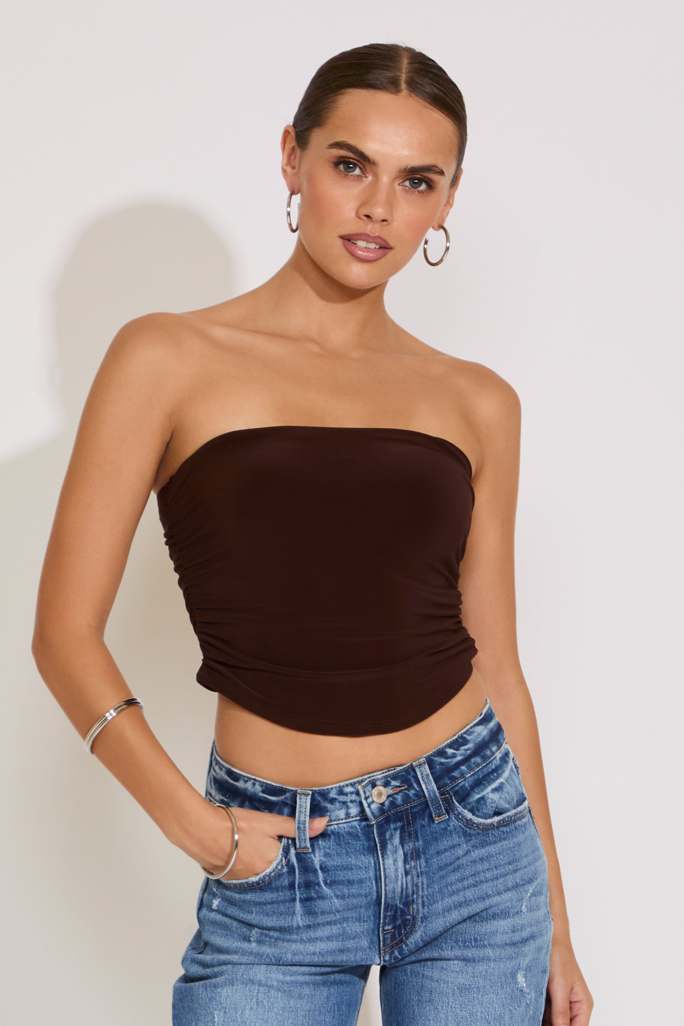 Woman wearing a brown strapless top and blue jeans against a plain background