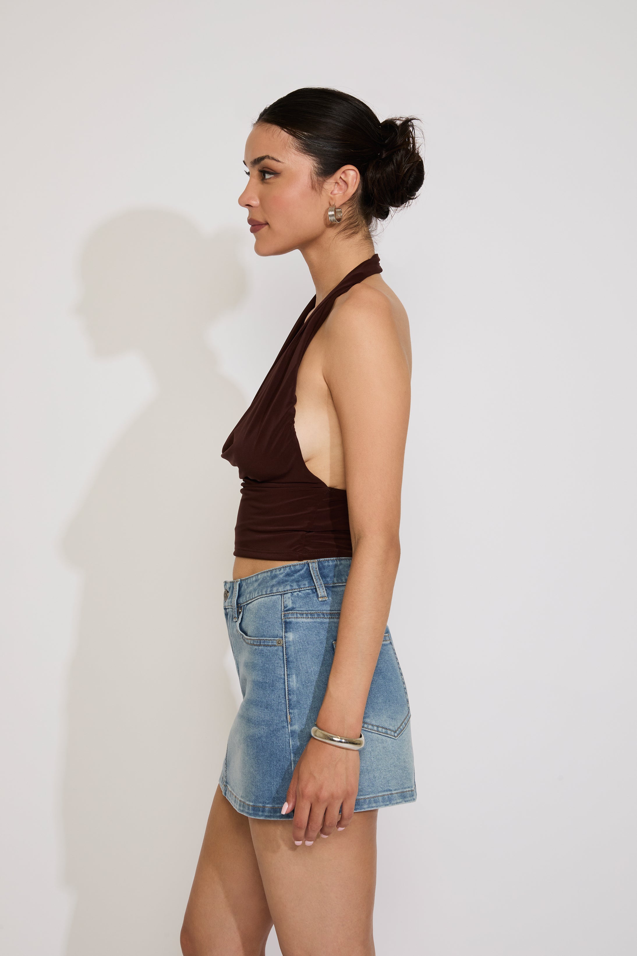 Woman wearing a brown halter top and denim skirt against a white background