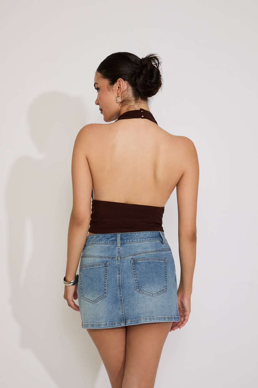 Woman wearing a green halter top and denim skirt against a white background