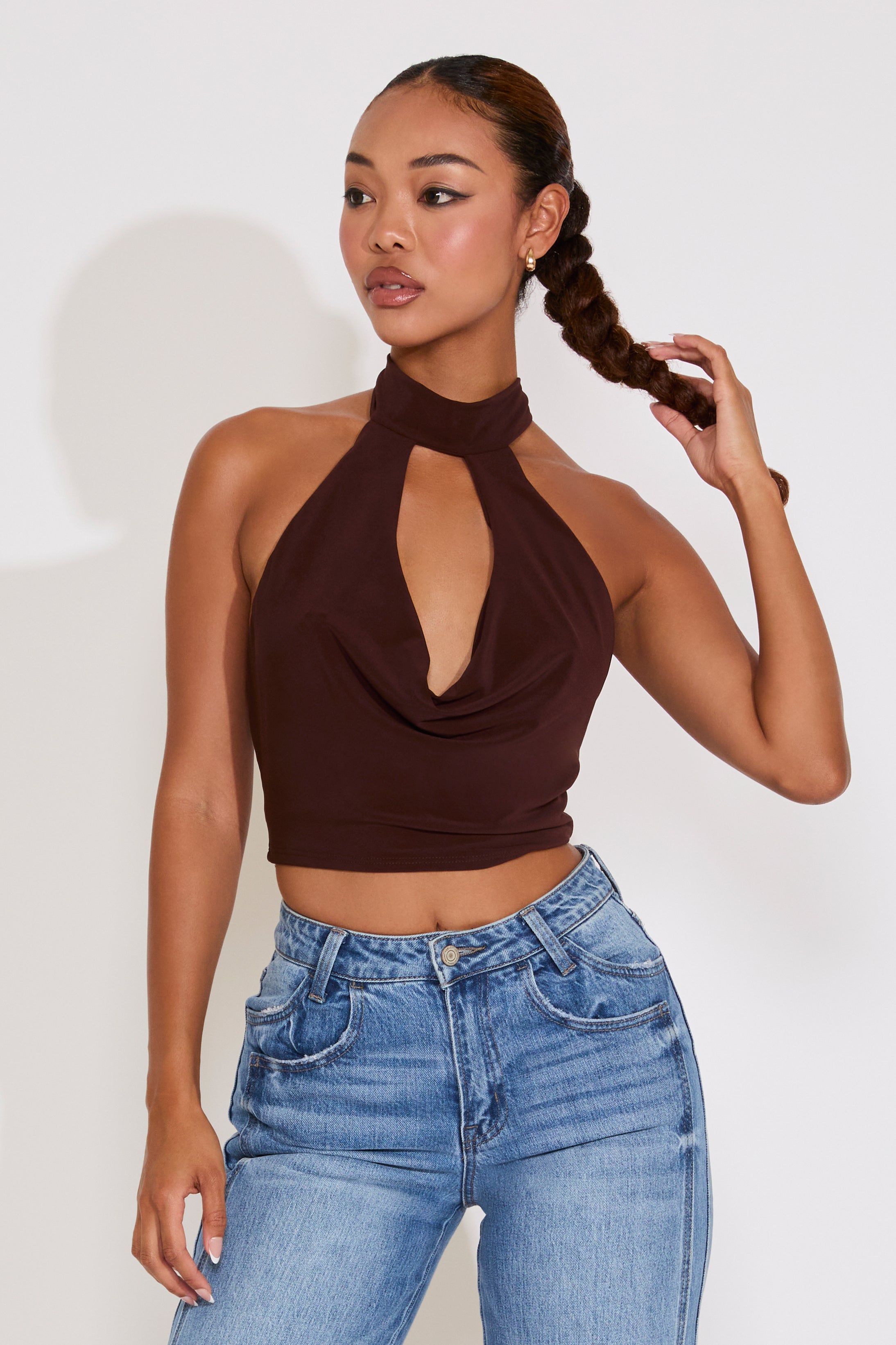 Woman wearing a brown halter top and blue jeans against a white background