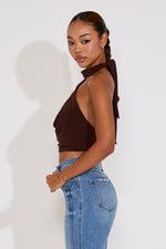 Woman wearing a brown halter top and blue jeans against a white background